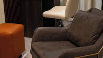 A modern room with a dark wooden desk, a white chair, an orange ottoman, and a lamp.