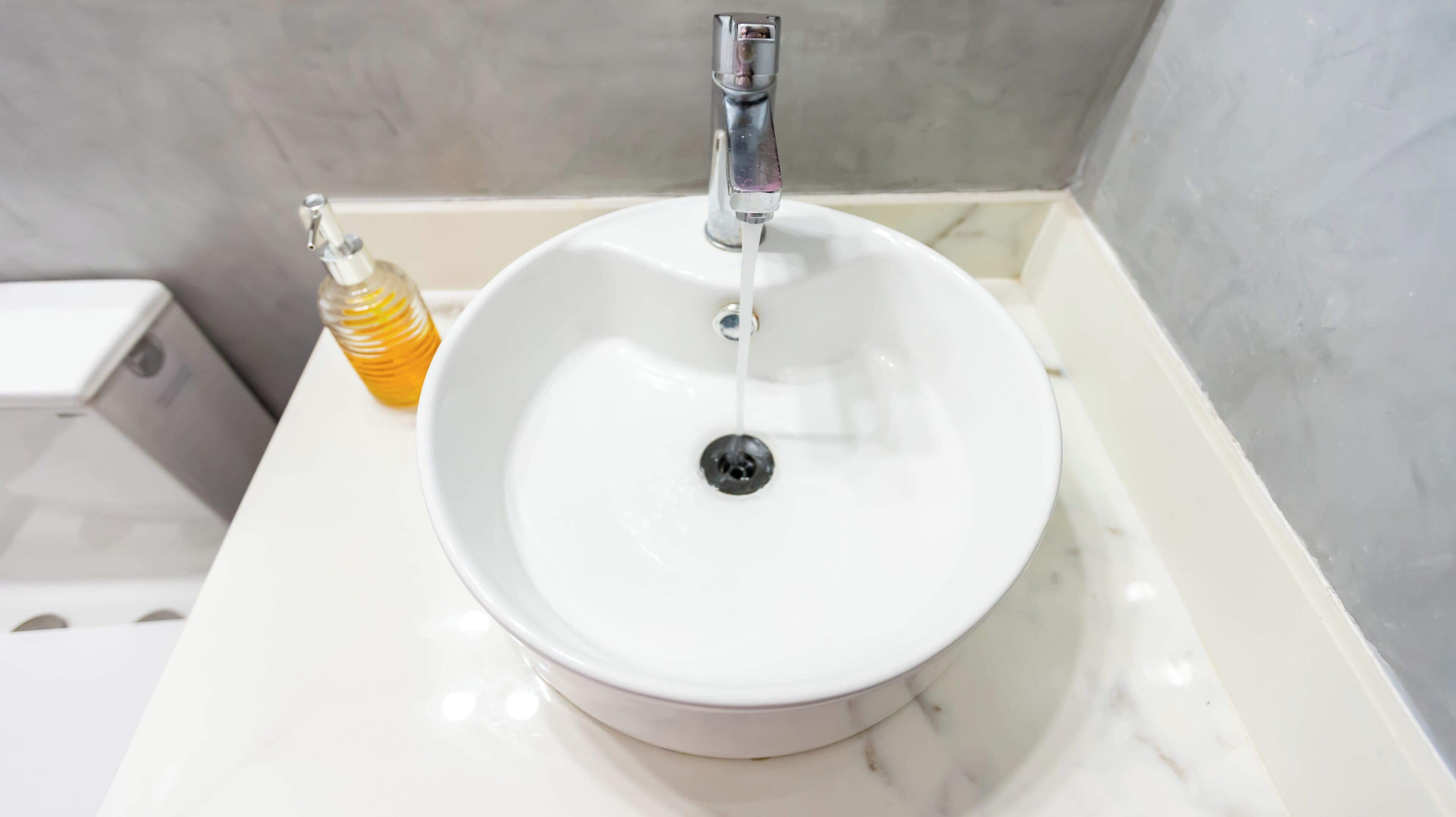 A white bathroom sink with a chrome faucet, a soap dispenser, and a toilet in the background.