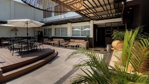 Ein moderner Außenbereich mit Tischen, Stühlen, einer Pergola und Kübelpflanzen.