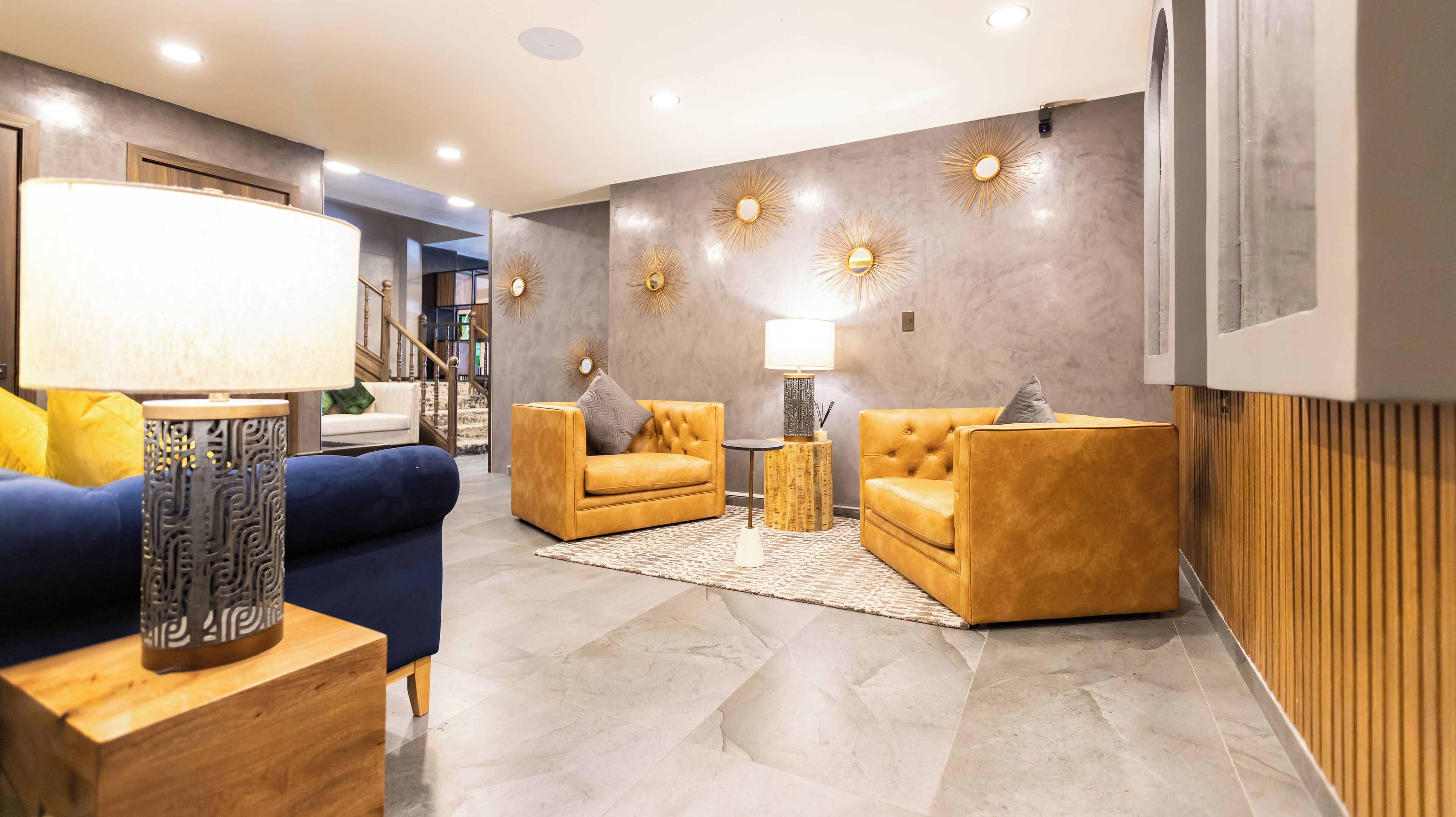 Un salon moderne avec un canapé bleu, deux fauteuils jaunes et une table d’appoint à motifs.