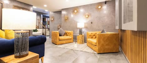 Un salon moderne avec un canapé bleu, deux fauteuils jaunes et une table d’appoint à motifs.