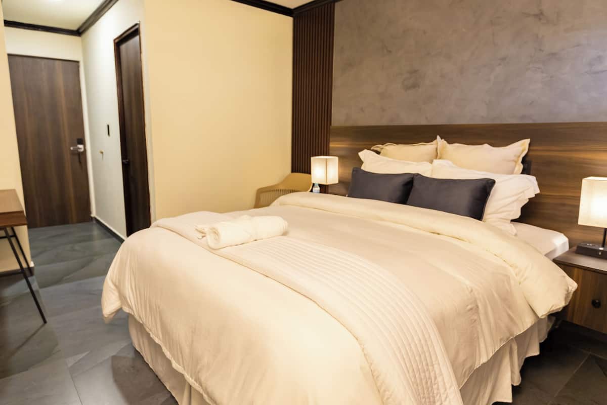 A hotel room with a large bed, bedside tables, a desk, and a lamp.