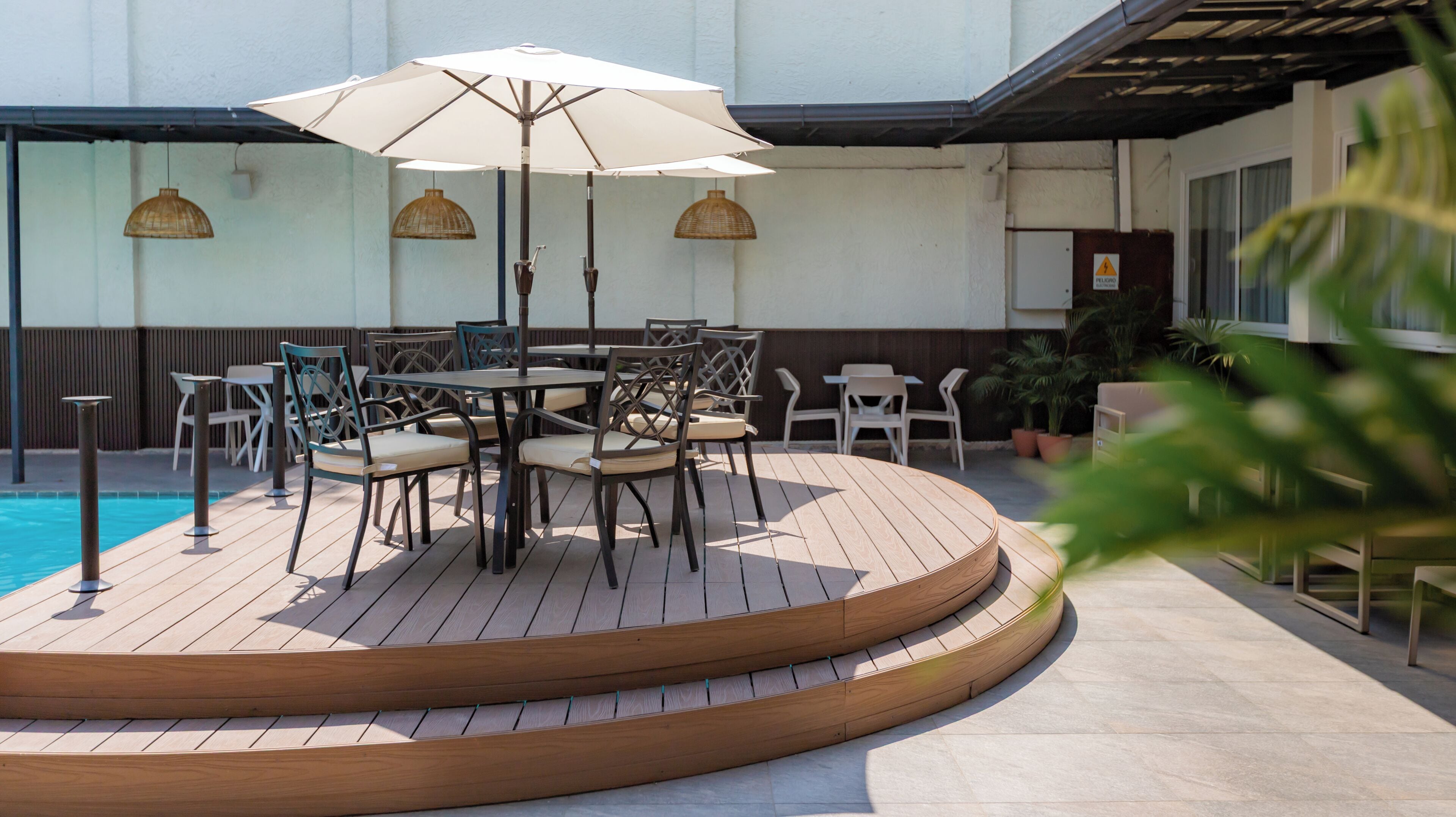 Un espace aménagé au bord de la piscine, avec une terrasse en bois, des sièges d’extérieur et un grand parasol.