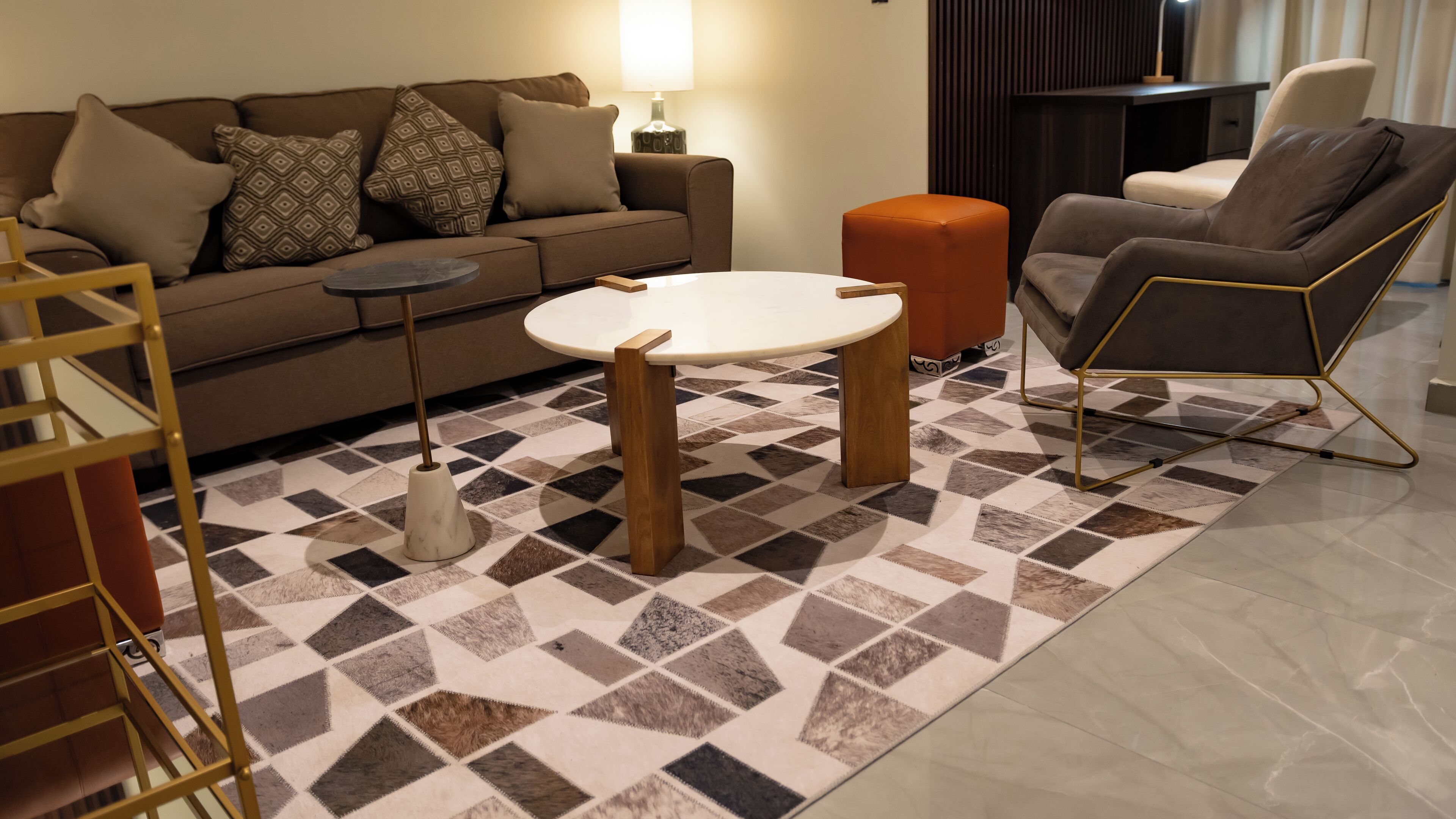 A living room with a sofa, a coffee table, an orange ottoman, and a chair.
