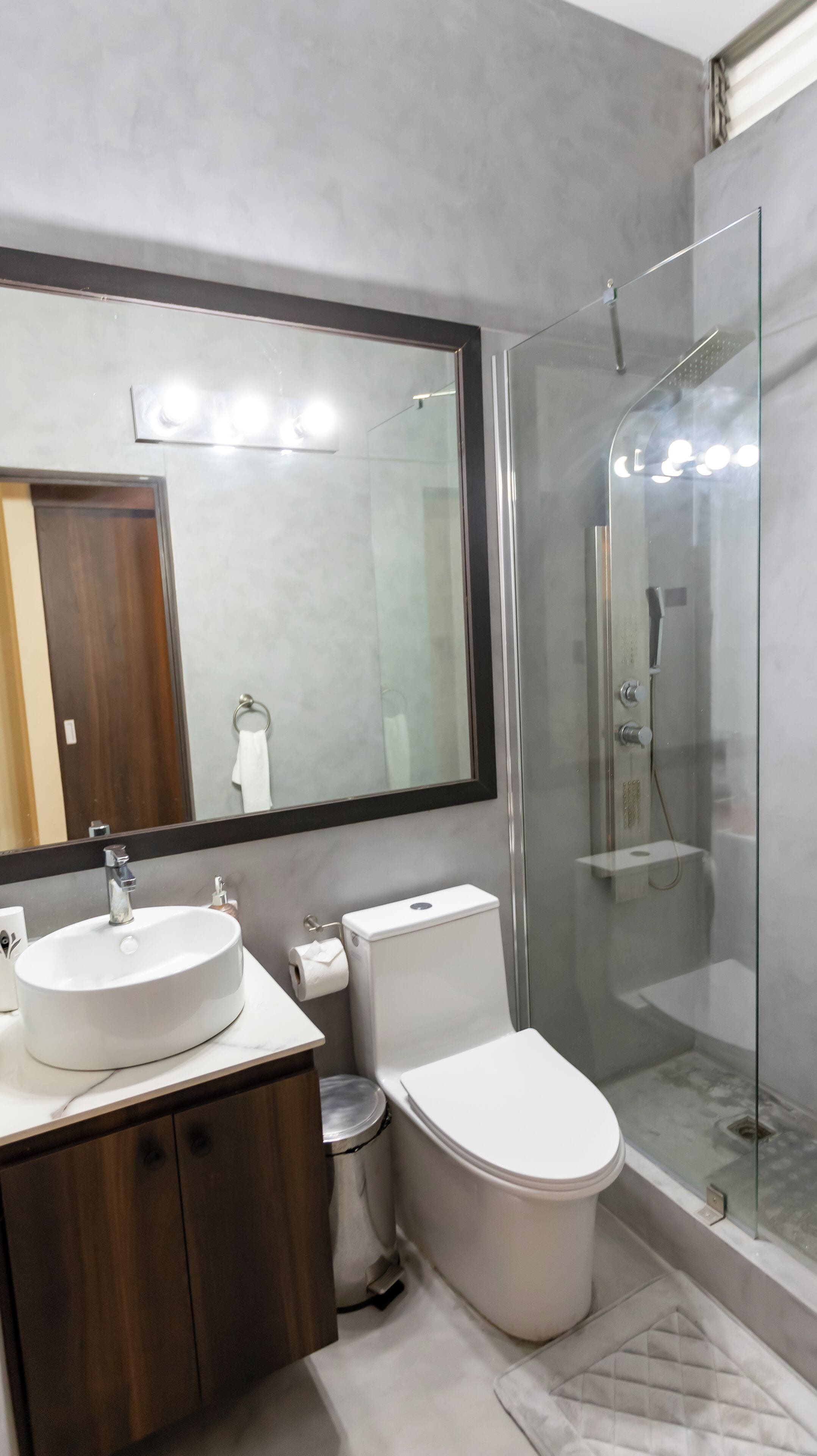 Et moderne badeværelse med et stort spejl, vask, toilet og en brusekabine i glas.