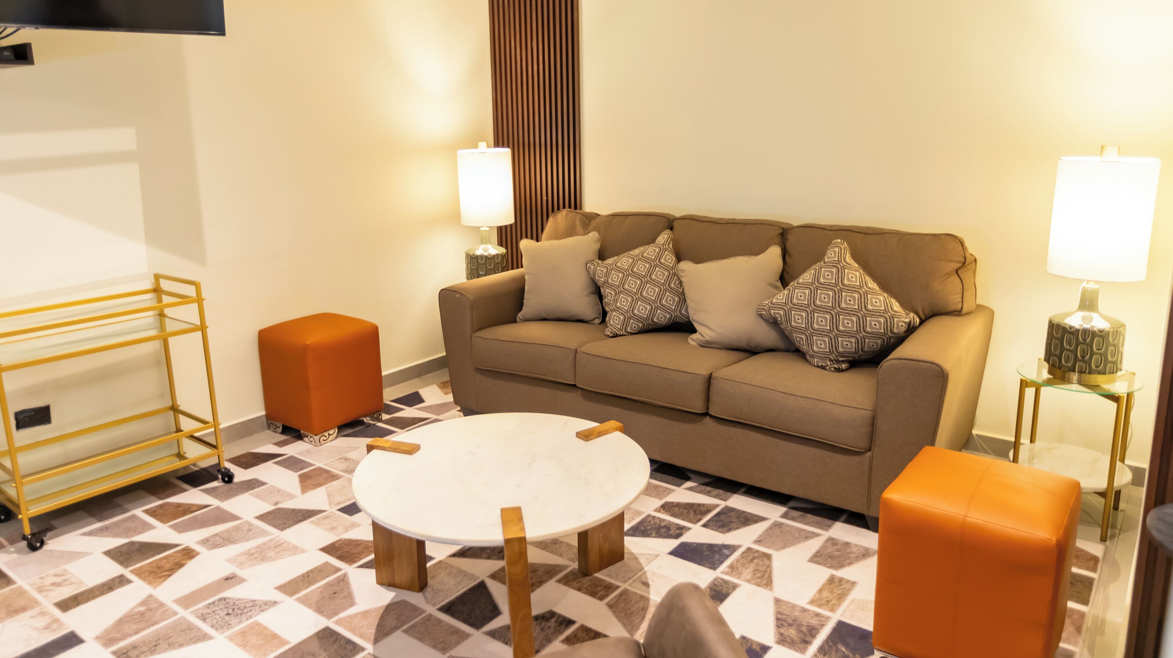 A living room with a sofa, two ottomans, a coffee table, a TV, and a lamp.