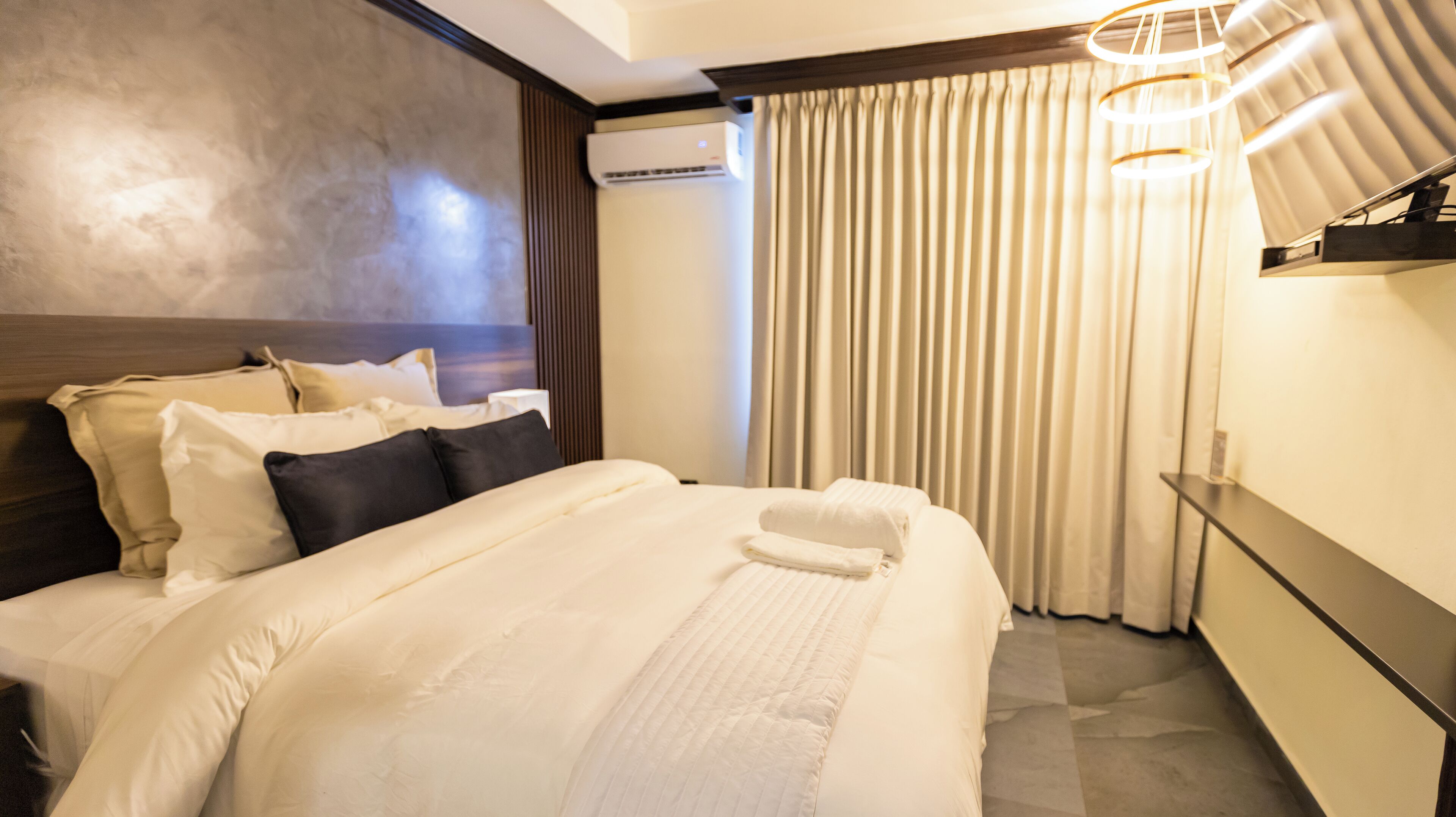 Une chambre d’hôtel avec un grand lit, une table de chevet, un climatiseur fixé au mur et une fenêtre avec des rideaux.