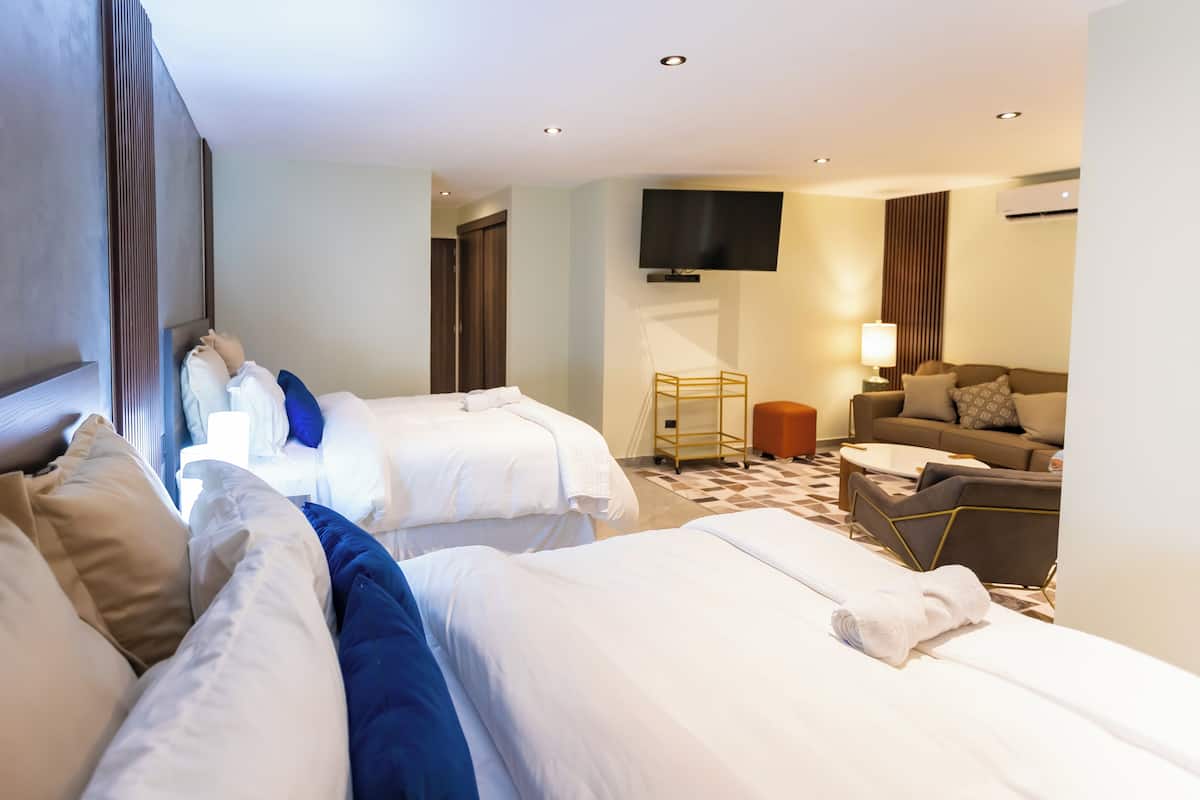 A hotel room with two beds, a sofa, a TV, and a lamp.