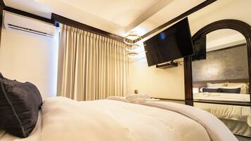A hotel room with a bed, a large mirror, a flat-screen TV, and a ceiling light fixture.