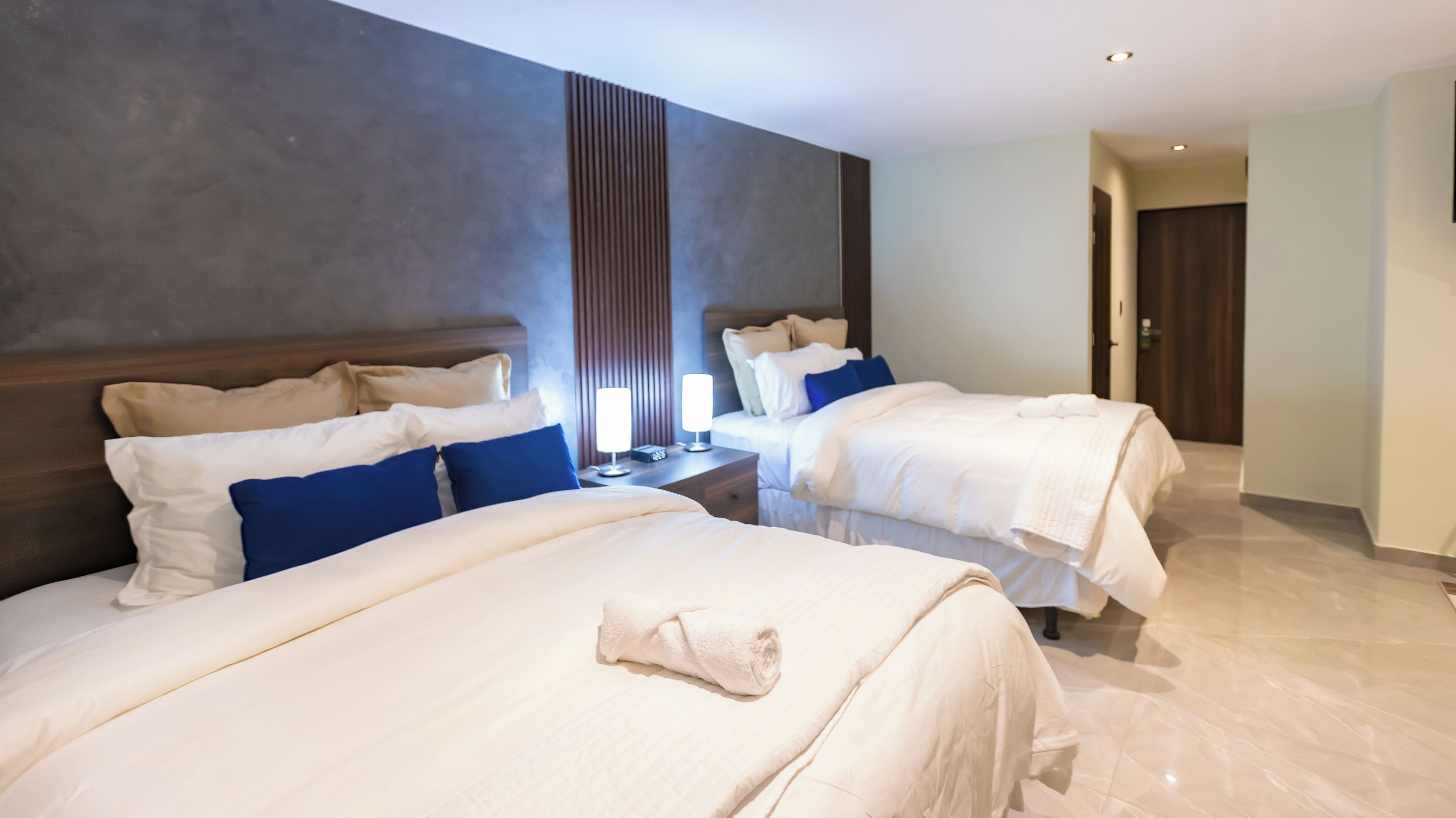 Una habitación de hotel con dos camas, una mesita de noche y una lámpara de pared.