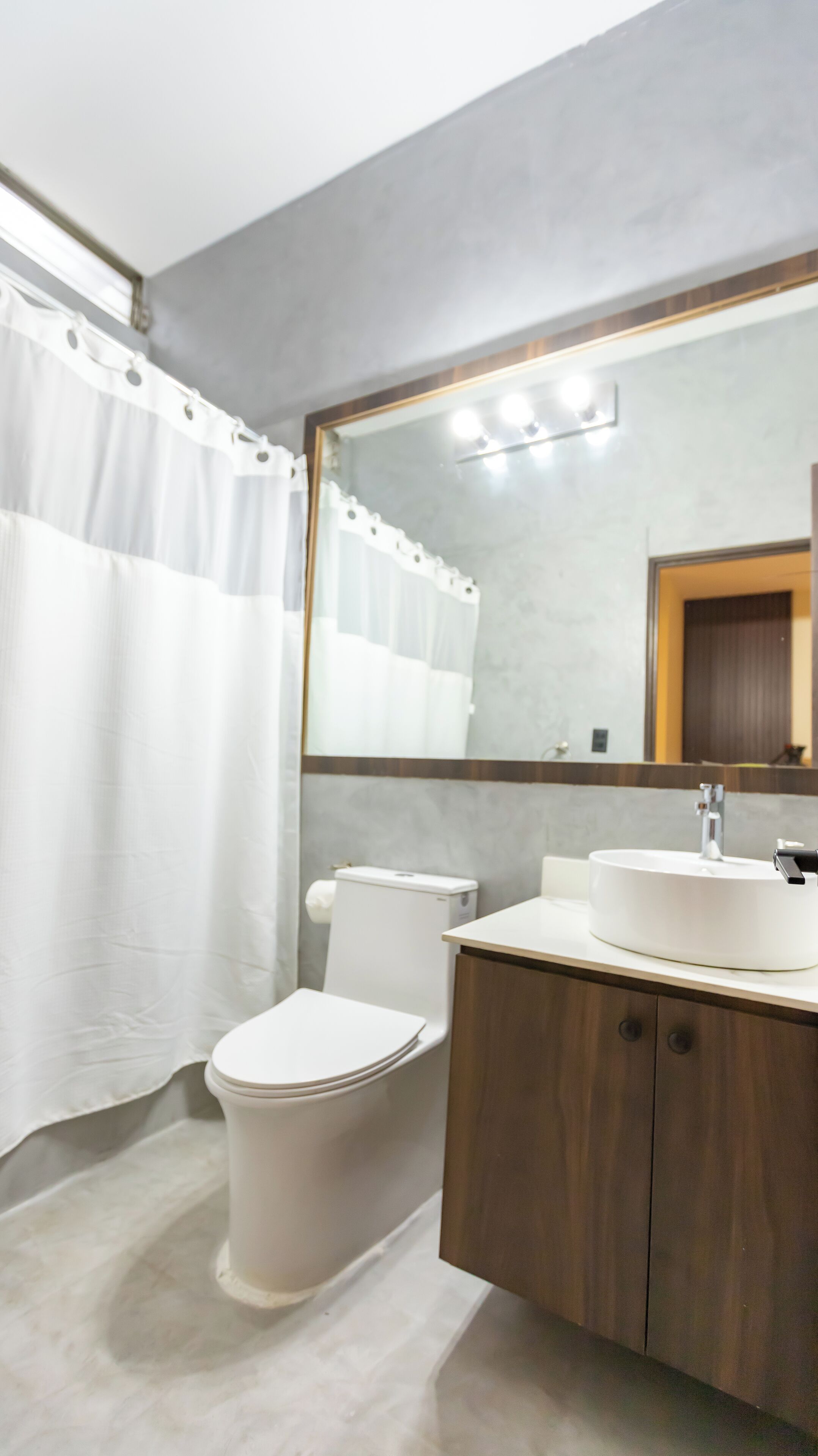 Ein modernes Badezimmer mit Toilette, Holzwaschtisch und großem Spiegel.