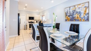 Una cocina moderna con armarios blancos, un refrigerador negro y un comedor con mesa de vidrio y sillas negras.