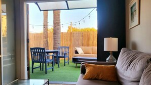 A living room with a glass table, a sofa with a cushion, a lamp, and a view of an outdoor patio with a table and chairs. - Indoor and Outdoor Living (Los Angeles)
