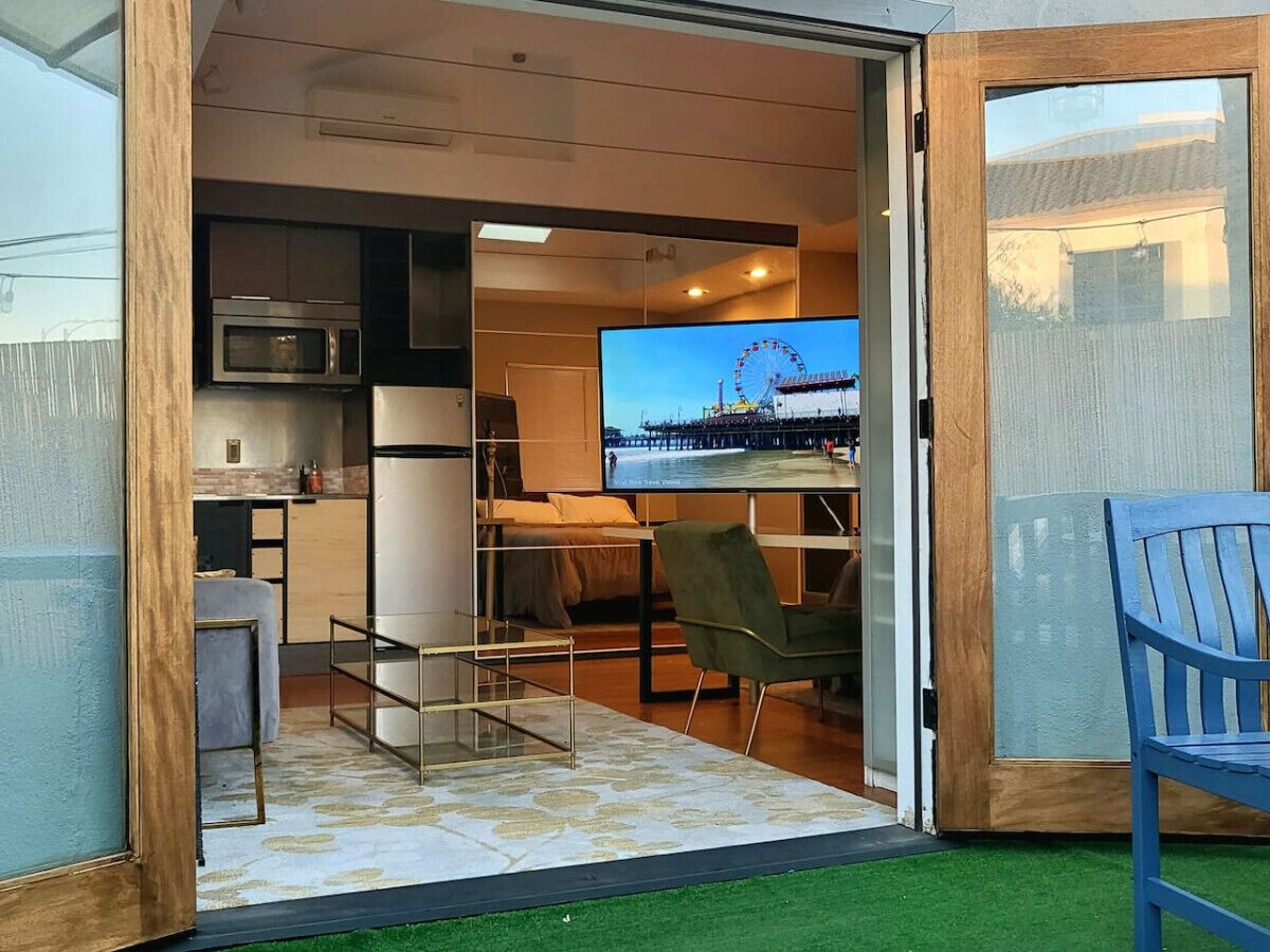 A compact living space with a kitchenette, a dining area with a TV displaying a Ferris wheel, and a small seating area with a chair.