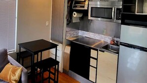 A compact kitchen with a microwave, oven, and refrigerator. There is a small dining table and a chair. - Indoor and Outdoor Living (Los Angeles)