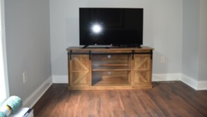 A room with a wooden entertainment center, a flat-screen TV, and hardwood flooring.