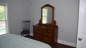 A bedroom with a bed, dresser, chair, and a door.