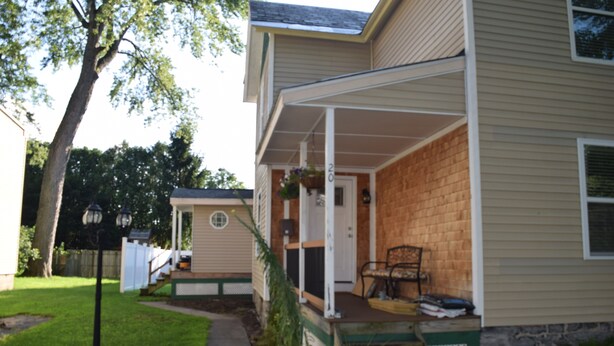 A two-story house with a covered porch, a front door, and a small front yard with a pathway.