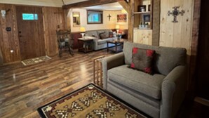 A cozy living room with a ceiling fan, wooden walls, a sofa, and a patterned rug.