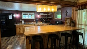 A kitchen with wooden flooring, a central island with stools, and a hanging light fixture.