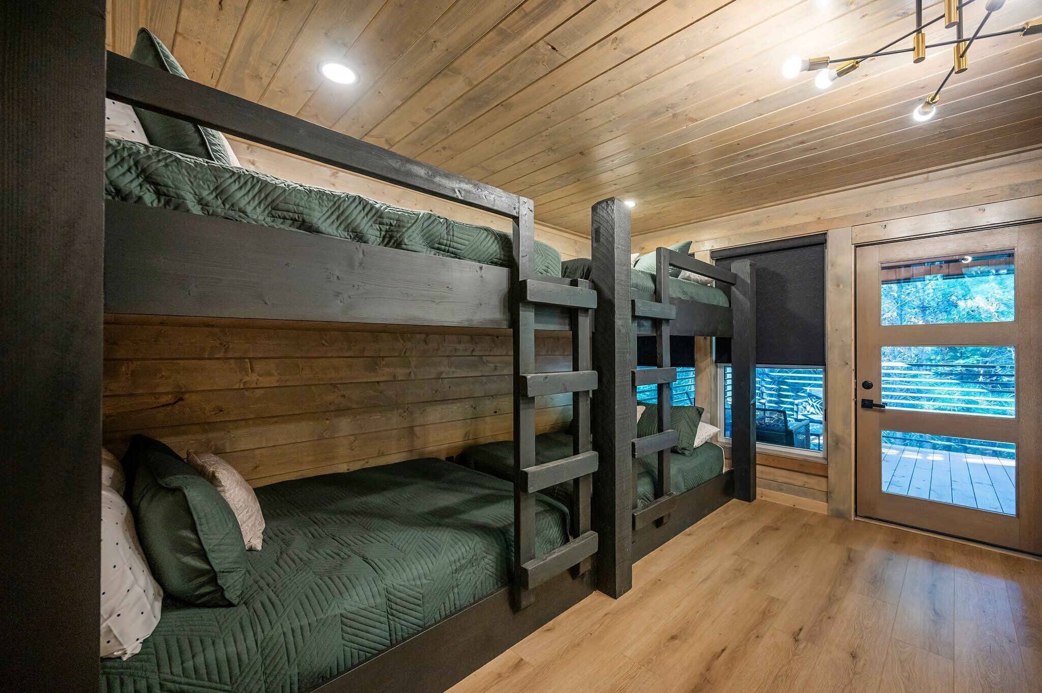 Une chambre avec des lits superposés, des murs en bois et une porte donnant sur une terrasse extérieure.