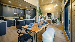 A modern kitchen with dark cabinets, a wooden dining table set with bowls, and a large island. - A Point in Time: Sleeps 12-16 | Fire Pit | Hot Tub (Broken Bow)