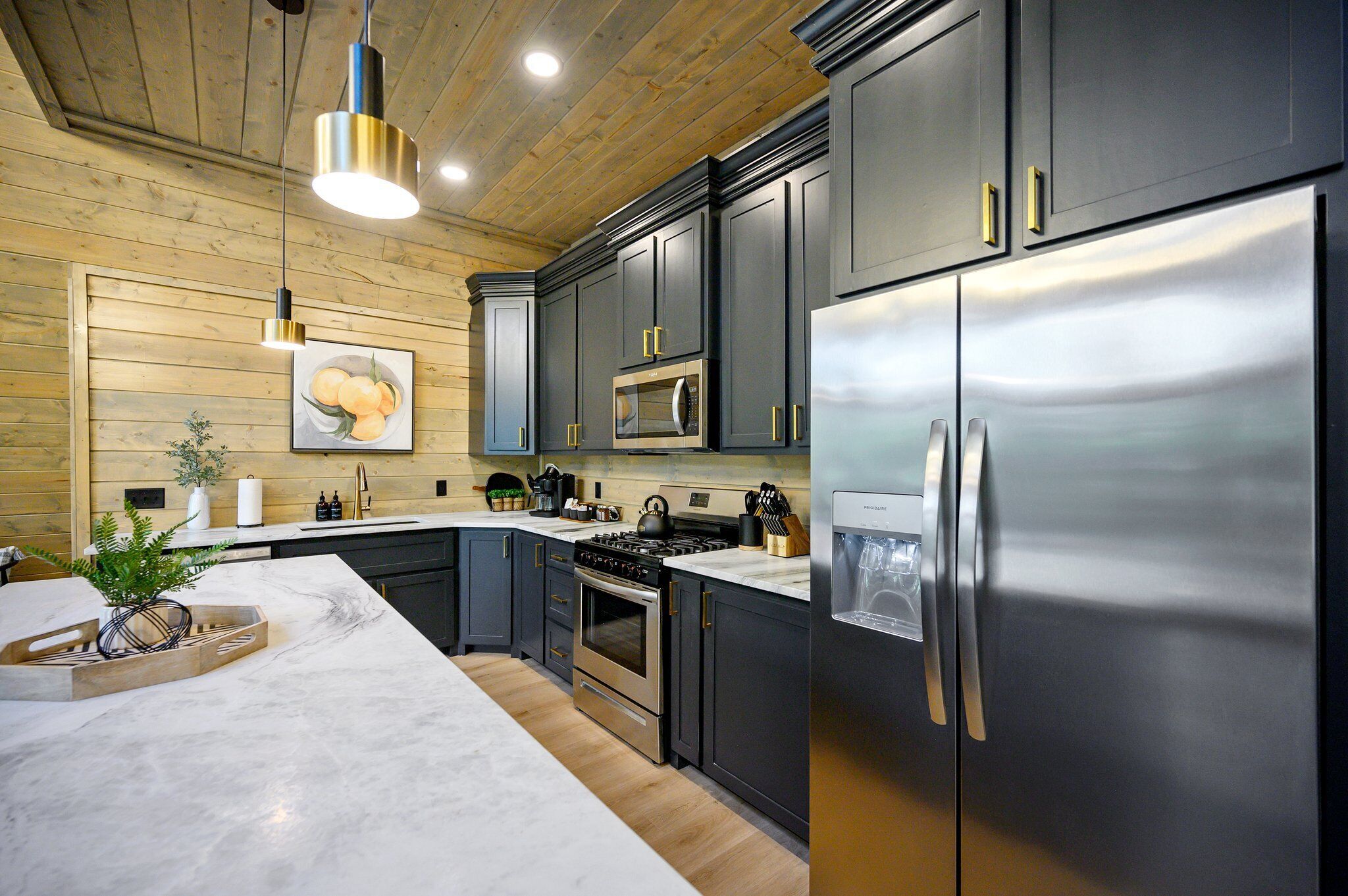 A modern kitchen with dark cabinetry, stainless steel appliances, and a wooden ceiling.