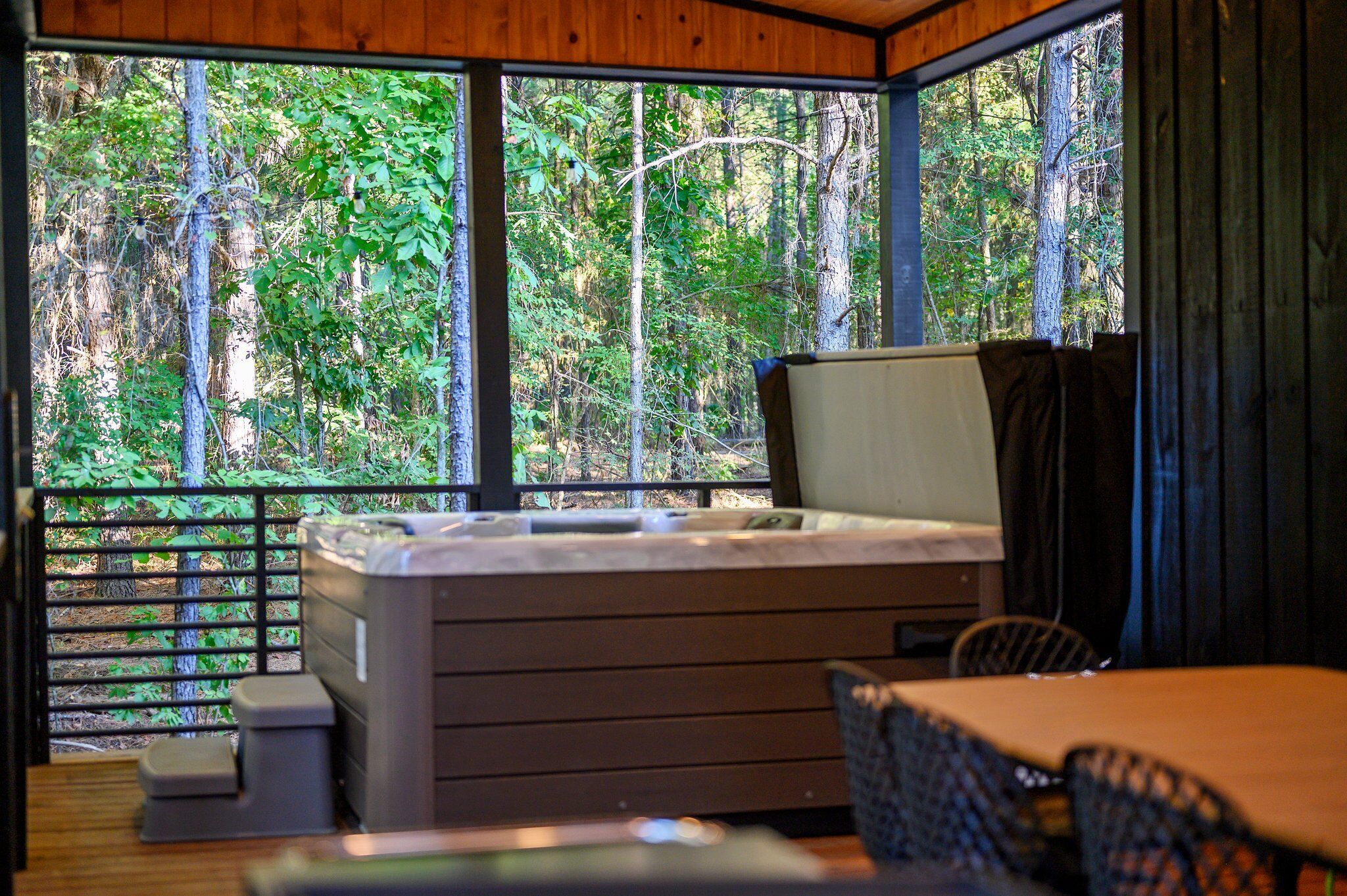 A cabin with a hot tub, a dining area, and a view of a forest.