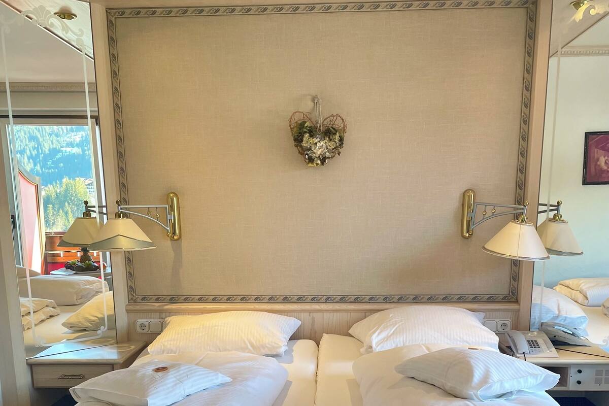 Habitación de hotel con una cama grande, dos mesitas de noche, un espejo y vistas al exterior.
