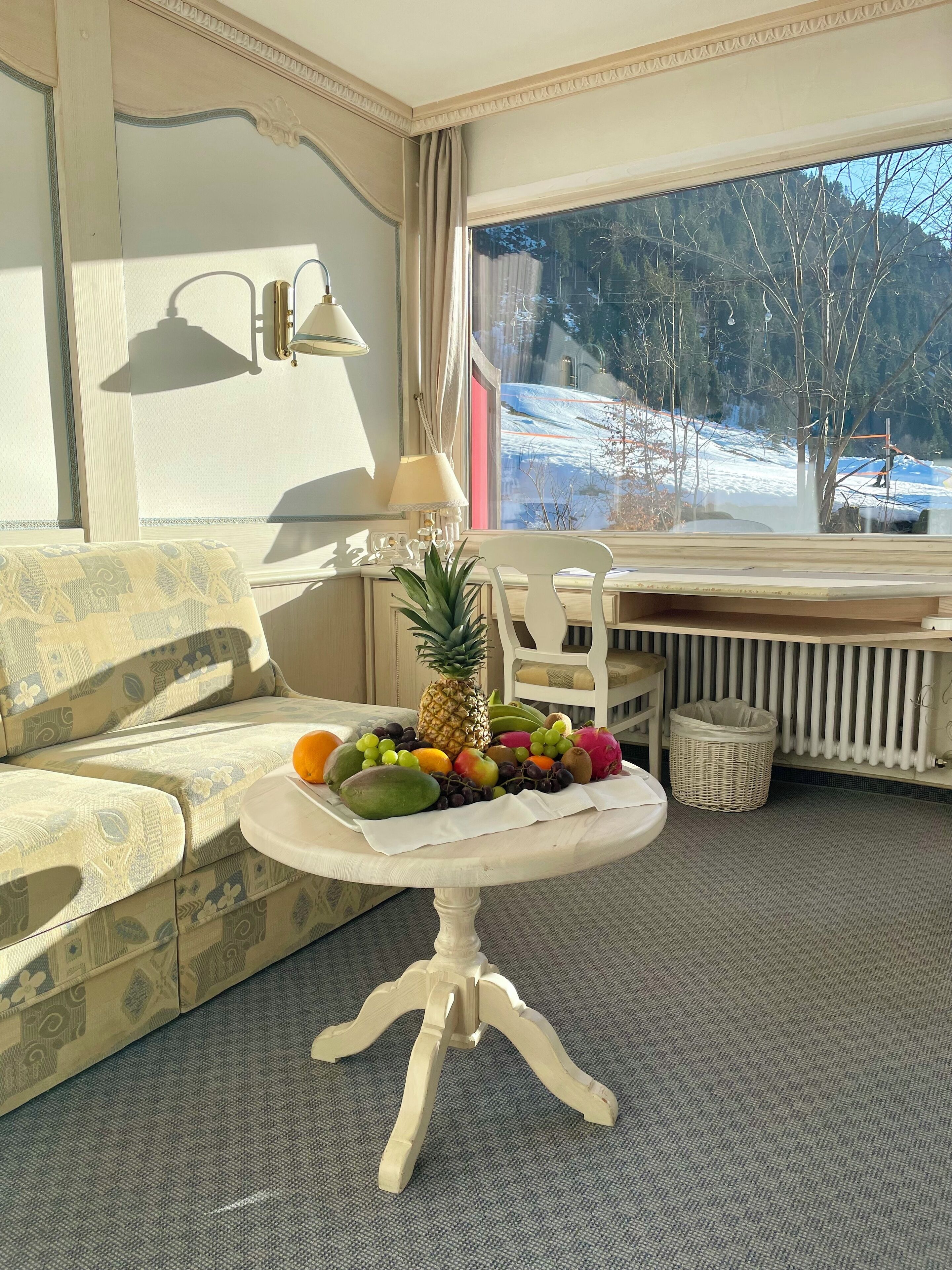 A room with a sofa, a table with fruit, a window with a snowy view, and a radiator.