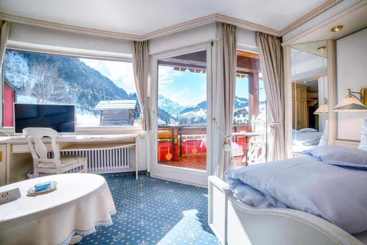Habitación de hotel con cama, escritorio y vistas a montañas.