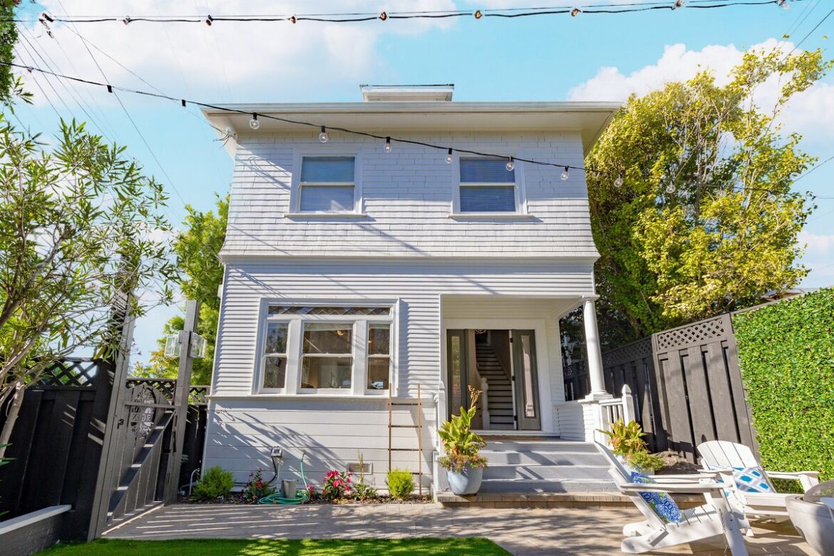 A two-story house with a front porch, a small garden, and a string of lights.
