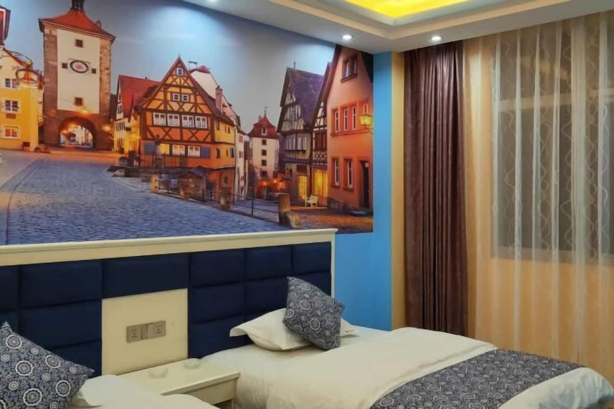 Un dormitorio con un mural de un pueblo europeo, una cama con ropa de cama estampada y una ventana con cortinas.