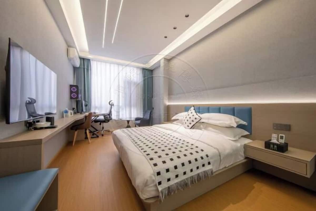 Una habitación de hotel moderna con una cama bien hecha, un escritorio con silla, un televisor de pantalla plana y una mesita de noche con lámpara.