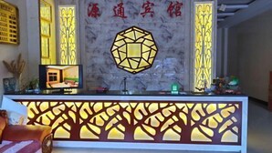 A reception desk with a geometric light fixture, a television, and a decorative wall with Chinese characters. - Xuanwei Yuantong Hotel (Xuanwei)