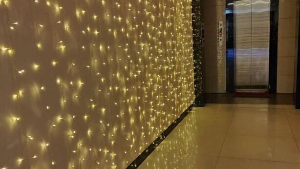 A corridor with a wall decorated with string lights and an elevator in the background. - Xuanwei Yuantong Hotel (Xuanwei)