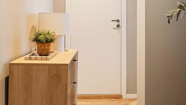 A hallway with a wooden cabinet, a lamp, and a door.