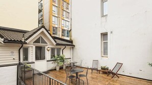 A courtyard with a wooden deck, outdoor seating, and a white building with a tiled roof.