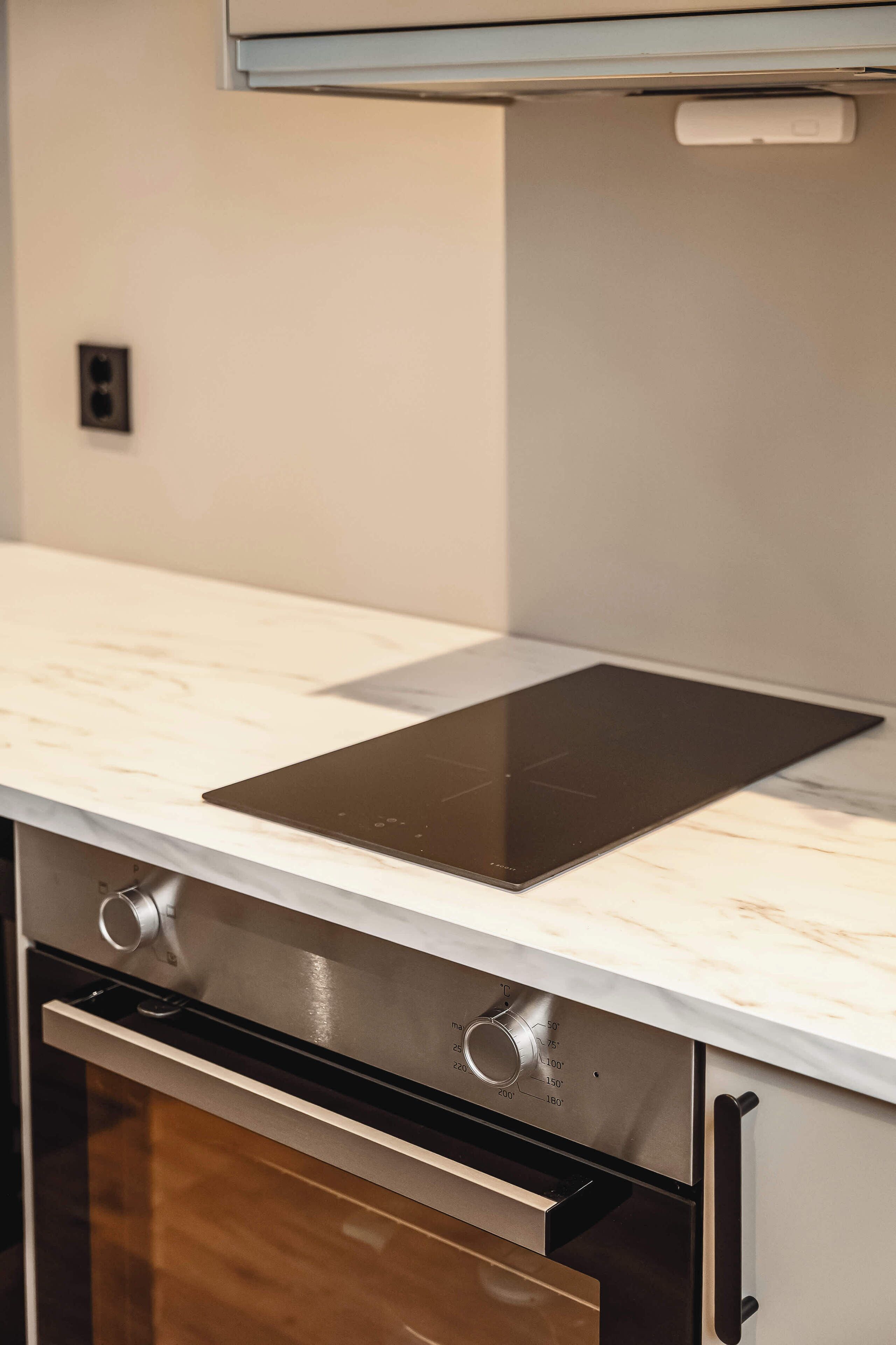 A kitchen with a built-in induction cooktop, a stainless steel oven, and a marble countertop.