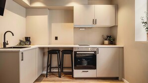 A compact kitchen with a built-in oven, two bar stools, a sink, and a window with a plant.