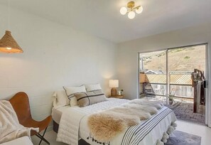 A bedroom with a bed, a chair, a lamp, and a view of the outside. - Sea House Dillon Beach - 2 Bed, 1 Bath - 5 Minute Walk To Beach (Dillon Beach)