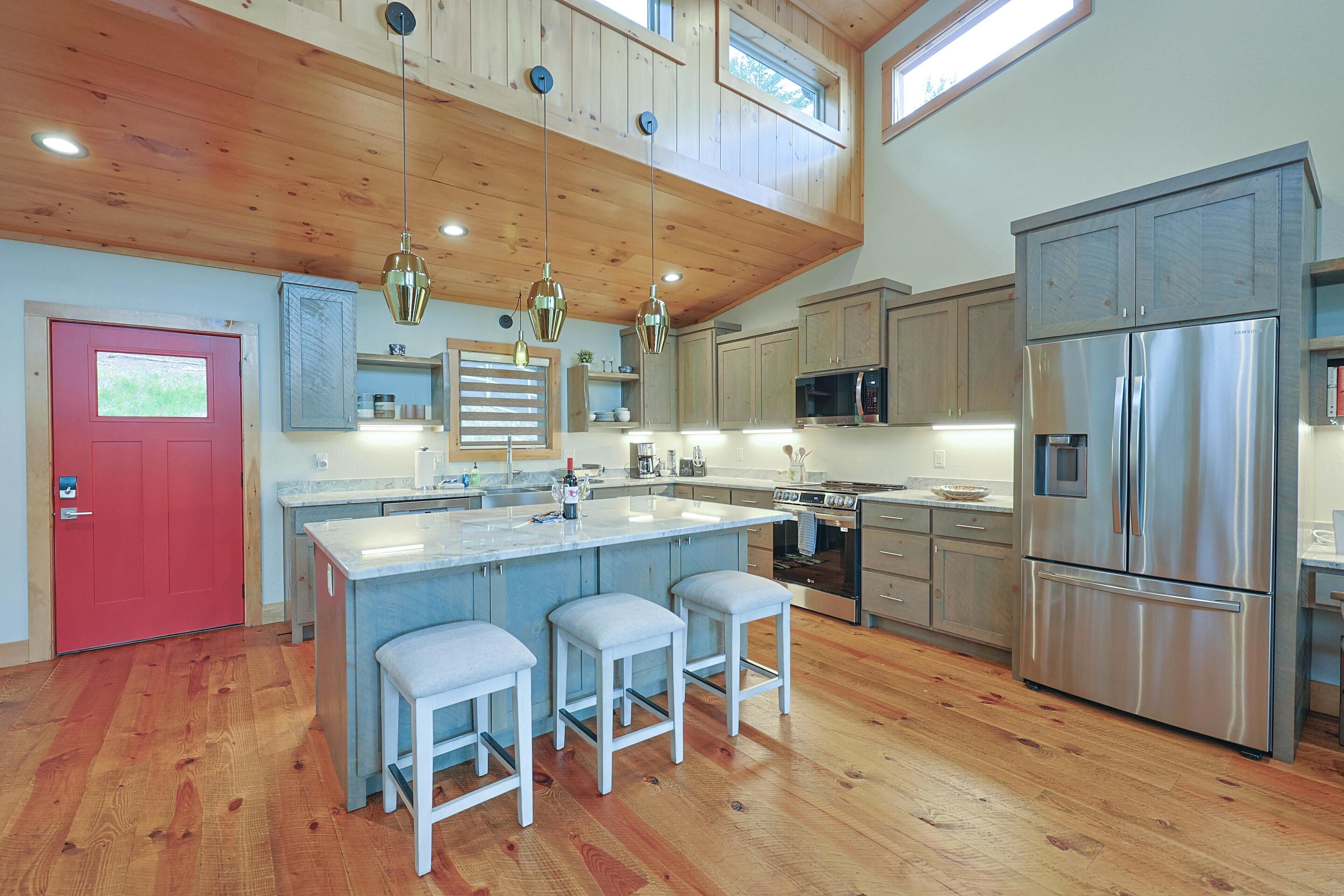 A modern kitchen with wooden ceiling, stainless steel appliances, and a red door.
