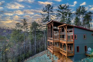 A multi-level wooden cabin with a balcony, surrounded by forest.