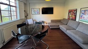 Ein modernes Wohnzimmer mit Glastisch, grauem Sofa und Kunstwerken an den Wänden.