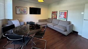 Ein modernes Wohnzimmer mit Glastisch, zwei Sofas, einem Flachbildfernseher und Kunstwerken an den Wänden.