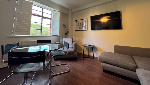 Ein modernes Wohnzimmer mit Esstisch, Stühlen, einer Couch, einem Fernseher und einem Fenster mit Jalousien.