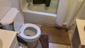 A bathroom with a toilet, bathtub, and shower curtain. - Newark's Art Deco 1-bdrm Oasis (Newark)