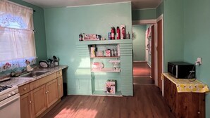 A compact kitchen with wooden cabinets, a sink, and a stove. There is a microwave on a wooden counter, and a small shelf with various items. - Newark's Art Deco 1-bdrm Oasis (Newark)