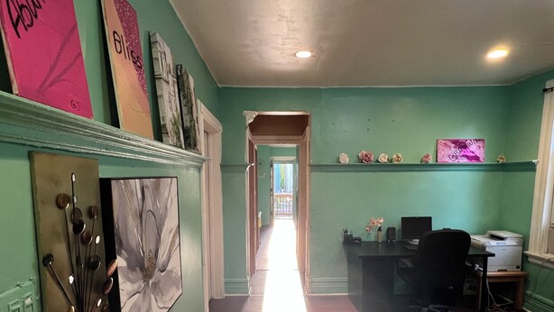 A room with a desk, chair, and a computer. There is a window with curtains, a door leading to another room, and a wall with framed pictures. - Newark's Art Deco 1-bdrm Oasis (Newark)