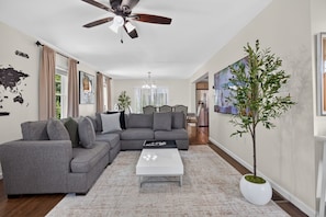 Un salon comprenant un canapé d’angle, une table basse, un ventilateur de plafond, une carte du monde accrochée au mur et une plante en pot.